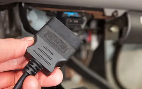 Dłoń trzyma adapter OBD II, gotowy do podłączenia i sprawdzenia kodu błędu w samochodzie.