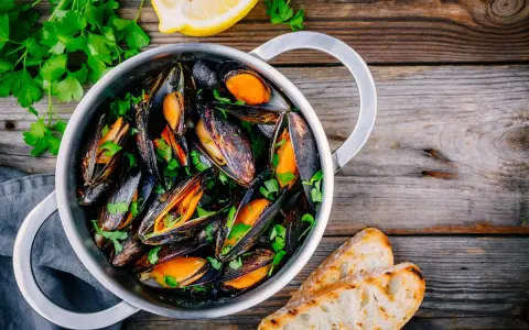 Un pentolino di cozze alla marinara, guarnite con prezzemolo fresco e accompagnate da fette di pane tostato e spicchi di limone.