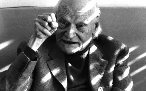 Ritratto di un anziano con pugno alzato, in memoria di Ungaretti. Le rughe sul volto e la luce che lo illumina creano un'atmosfera intensa.