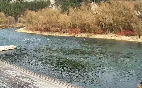 Szeroka rzeka płynie wśród drzew i skalistych zboczy.