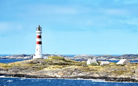 Rött och vitt fyr på en klippig ö nära Kristiansand, Norge. Små vita hus ligger utspridda på ön.