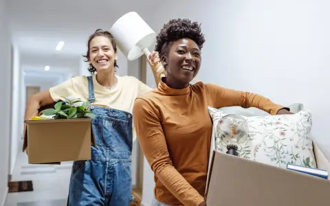 Deux amies souriantes déménagent, portant des cartons remplis d'objets. Une nouvelle aventure commence, peut-être grâce à un **bail solidaire**.