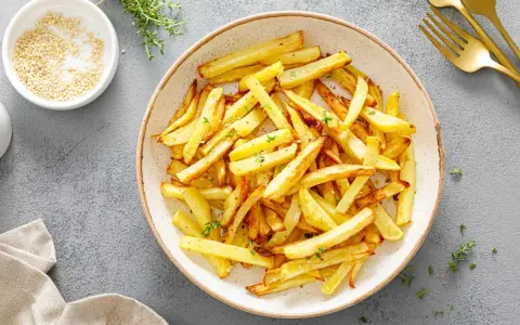 Un plato lleno de crujientes patatas fritas doradas, espolvoreadas con hierbas frescas. ¡Perfectas para compartir!