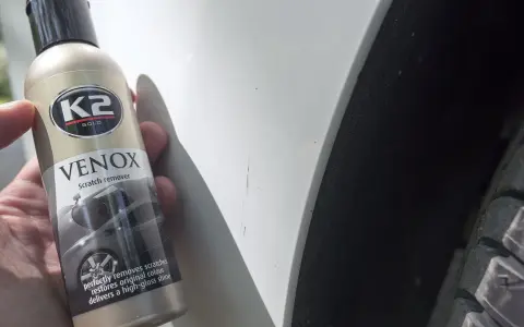 Jak usunąć głębokie rysy na lakierze? Butelka K2 VENOX Scratch remover obok białego lakieru z widocznymi zarysowaniami.