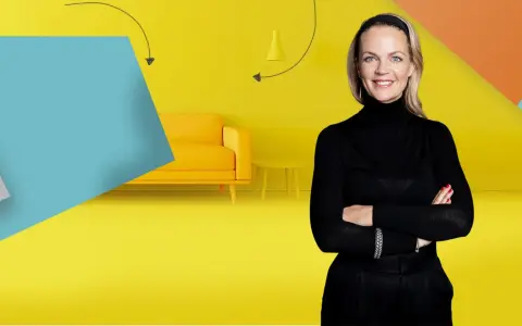 Frau mit Armen verschränkt vor gelbem Hintergrund mit Sofa und Beistelltisch. Inspiration für Renovierungs Serien Deutsch.