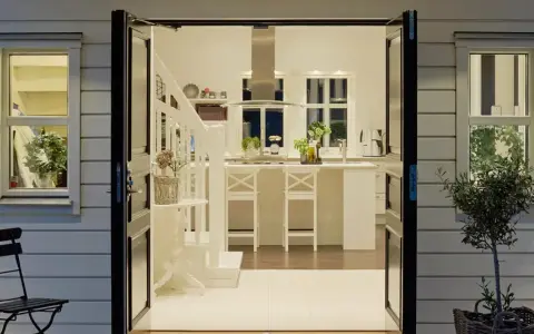 Välkomnande entré inspiration utomhus. Öppna dörrar leder in till ett ljust kök med köksö och trappa.