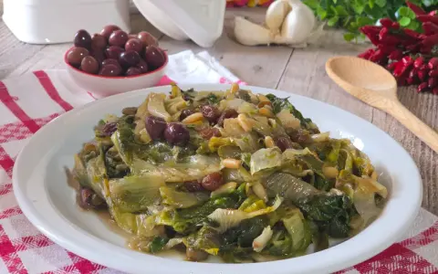 Scarola in padella con olive, pinoli e uvetta, un contorno saporito e colorato.