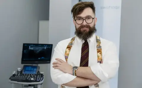 Ortopeda w okularach i ozdobnych szelkach stoi przed aparatem USG.
