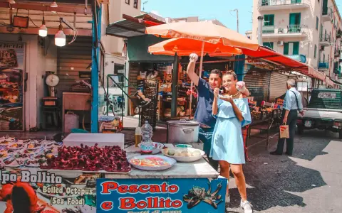 Coppia felice assaggia polpo fritto in un mercato di Palermo in un giorno di sole. Un assaggio autentico della Sicilia.