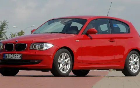 Czerwone BMW 116i z polskimi tablicami WI 3766G zaparkowane na czerwonym chodniku.