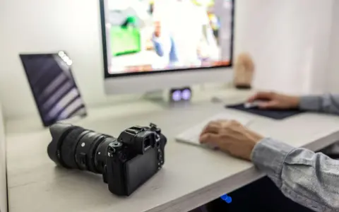 Aparat fotograficzny i tablet na biurku, obok komputera. Ułatwia to proces, jak przegrać zdjęcia z telefonu na komputer.