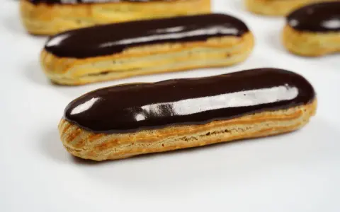 Plusieurs éclairs au chocolat brillants, avec un fondant pour éclair parfait, sont disposés sur fond blanc.