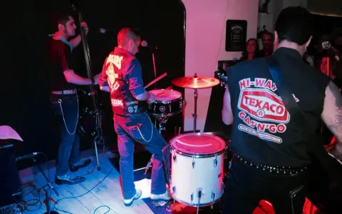 Un grupo de gatos locos en el escenario, tocando rock and roll con un contrabajo, batería y guitarra.