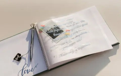 Otwarta księga gości z ozdobnym długopisem i napisem "love". Na otwartej stronie widnieją mądre życzenia ślubne od rodziców, ozdobione małym zdjęciem.
