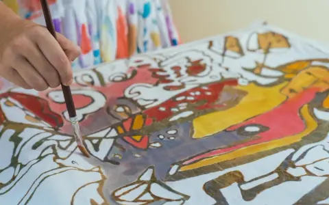 Ręka maluje pędzelkiem wzory na tkaninie, tworząc barwny obraz w technice papatya batik.