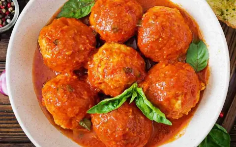Polpette di pane succulente in salsa di pomodoro, guarnite con foglie di basilico fresco. Un piatto che sa di casa.