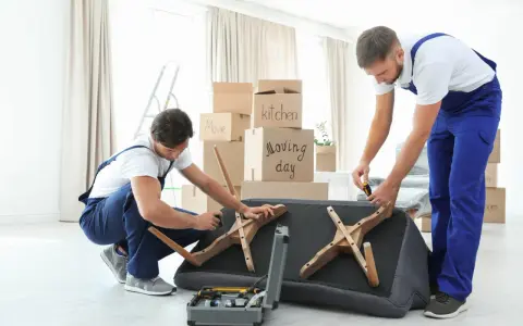 Deux déménageurs démontent un canapé fixe, outils à portée de main. Ils préparent le mobilier pour un déménagement.