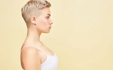 Perfil de una mujer joven con un moderno corte pixie rubio, luciendo un top blanco.