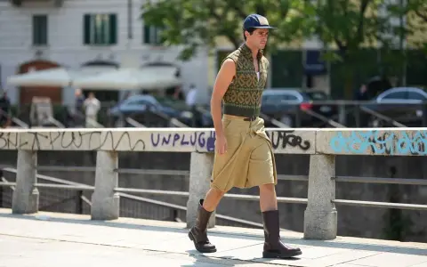 Uomo con un elegante outfit sportivo estivo: gilet a fantasia, bermuda color sabbia e stivali.