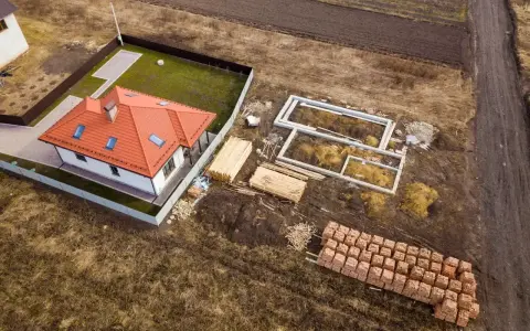 Działka rolno budowlana z gotowym domem i fundamentami pod kolejny. Materiały budowlane czekają na rozpoczęcie prac.