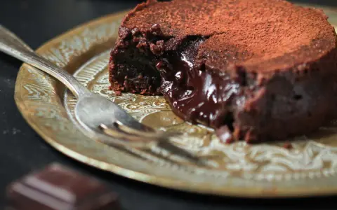 Fondant au chocolat cacao, cœur coulant, saupoudré de cacao, sur une assiette dorée avec une fourchette.