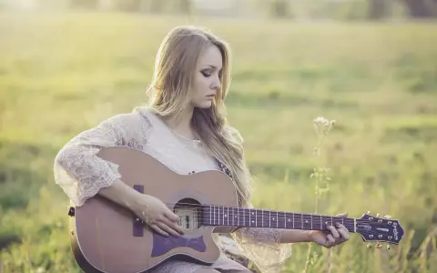 Blondynka w koronkowej sukience gra na gitarze w słonecznym polu. To jak remaster starych wspomnień, pełen ciepła i nostalgii.