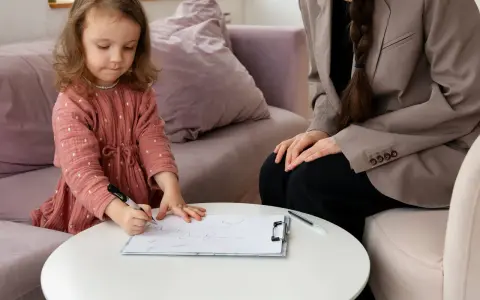 Mała dziewczynka rysuje, podczas gdy psycholog obserwuje. Proces ten może być częścią diagnozy ados.