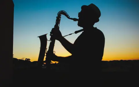 Sylwetka muzyka w kapeluszu grającego na saksofonie o zachodzie słońca. Prawdziwy mistrz, jeden z najlepszych bluesmanów świata.