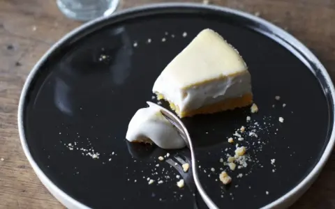 Un trozo de tarta de queso cremoso, con una porción ya probada, sobre un plato negro.