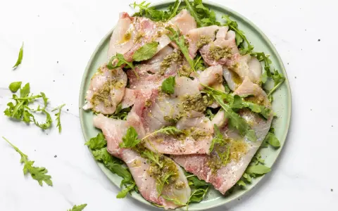 Deliziosi antipasti di pesce crudo, affettati sottili e conditi con erbe aromatiche e olio, serviti su un letto di rucola fresca.