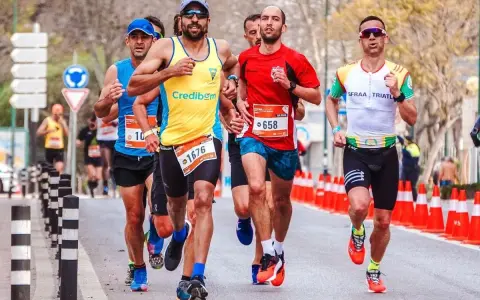 Atleti in gara, con pettorali visibili, corrono su strada. Le tabelle ripetute corsa principianti sono un ottimo modo per iniziare.