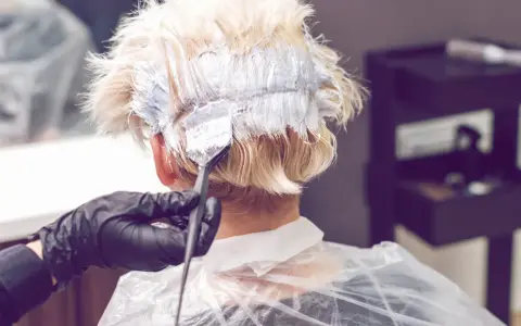 Friseur mit Handschuhen trägt Bleichmittel auf blondes Haar auf. Der Prozess des Haare bleichen beginnt.