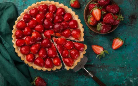 Une magnifique tarte aux fraises, garnie de fruits rouges brillants, est prête à être dégustée. Une part a été coupée, révélant la crème onctueuse.