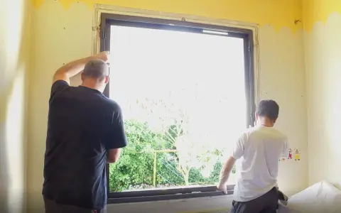 Deux hommes installent une nouvelle fenêtre, une étape clé dans la rénovation de cette pièce.