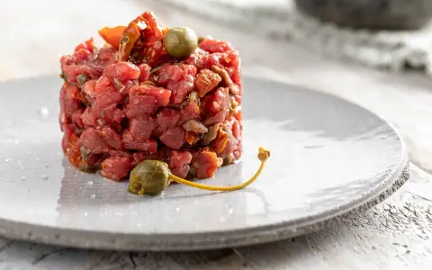 Deliziosa tartare di manzo, guarnita con capperi e pomodori secchi, servita su un piatto grigio.