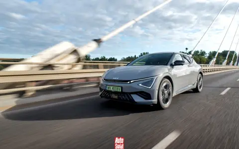 Szary Kia EV6 jedzie po moście w słoneczny dzień.