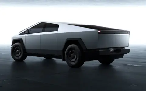 Futurystyczny Tesla Cybertruck w kolorze srebrnym, z ostrymi krawędziami i masywnymi kołami, prezentuje się na ciemnej, betonowej podłodze.