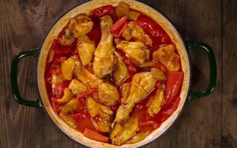Un saporito pollo con peperoni in umido, cotto in una casseruola verde su un tavolo di legno scuro.