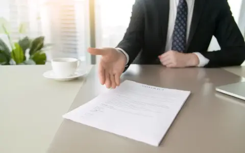 Biznesmen wyciąga rękę do uścisku nad dokumentem, symbolizującym rezygnację z pracy.