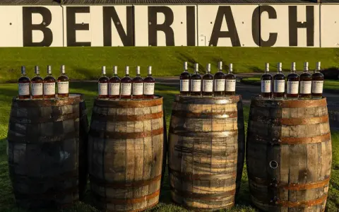 Butelki whisky Benriach stoją na beczkach, które czekają na dojrzewanie w pomieszczeniu.