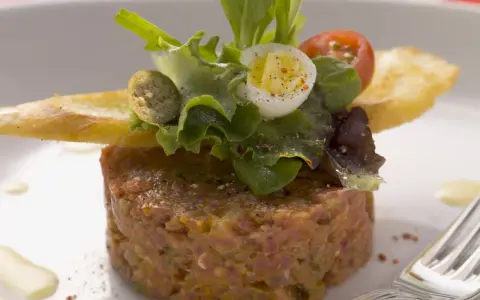 Un délicieux tartare de bœuf, garni d'une salade fraîche, d'un œuf de caille et de croûtons. Une recette parfaite pour un repas raffiné.