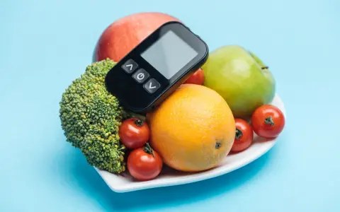 Zdrowa dieta dla cukrzyka: brokuły, pomarańcza, jabłka i pomidorki. Glukometr na talerzu.