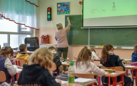 Nauczycielka dyplomowana pisze na tablicy, dzieci słuchają. Ciekawe, jakie nauczyciel dyplomowany zarobki ma w tej szkole.