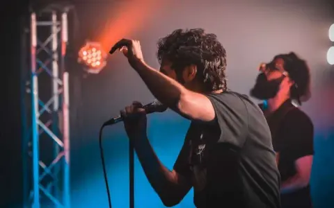 Ein Sänger mit Mikrofon auf einer Bühne, umgeben von Bühnenlichtern. Das ist, was Indie-Musik ausmacht: Leidenschaft und Energie.