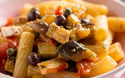Un piatto invitante di pasta con pesce, arricchito da olive nere, capperi e verdure colorate.