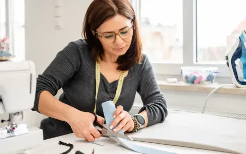 Une couturière utilise des ciseaux pour couper du tissu, montrant l'importance des différents types de ciseaux de couture pour un travail précis.