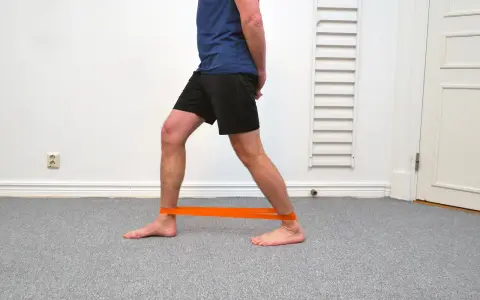 Man tränar för att stärka stela fotleder med ett orange träningsband runt anklarna.