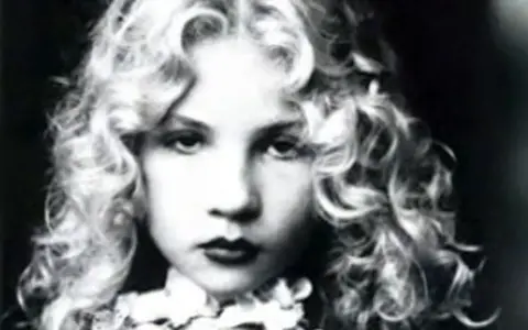 Portrait en noir et blanc d'Eva Ionesco enfant, aux boucles blondes et au regard intense.
