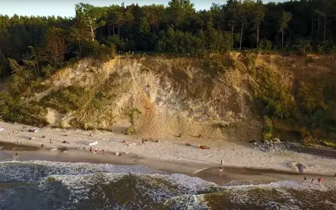 Plaża u stóp najwyższego klifu w Polsce. Ludzie spacerują po piasku, fale obmywają brzeg.