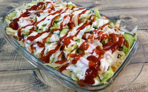 Kapsalon z kurczakiem, sałatą, pomidorami, ogórkiem i sosami w szklanej misce.